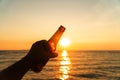 Hand of man is holding beer bottle and holds his hand up on the sky in evening with sunset. celebrating on holiday at the beach in Royalty Free Stock Photo