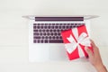 Hand of man holding gift box and having laptop computer on wooden table, present giving for Christmas day. Royalty Free Stock Photo