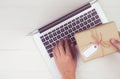 Hand of man holding gift box and tag having laptop computer on wooden table, present giving for Christmas day. Royalty Free Stock Photo