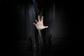 The hand of the man holding the stick from the wooden door from the inside of the dark