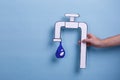 The hand of the man holds a paper image of the tap with a drop of water. Blue background. Royalty Free Stock Photo