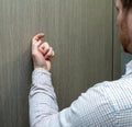 The hand of a man, in a light shirt in a business cage, knocks loudly on the door. Young man visitor Royalty Free Stock Photo