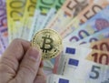 Hand of man with one big goden BITCOIN and euro banknotes on background