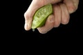 The hand of a man squeezes juice from half a lime. Juicy drop hanging down Royalty Free Stock Photo