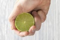 The hand of a man squeezes the juice from a slice of lime half. Juicy drop hanging down Royalty Free Stock Photo