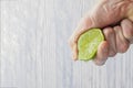 The hand of a man squeezes the juice from a slice of lime half. Juicy drop hanging down Royalty Free Stock Photo