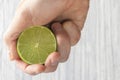 The hand of a man squeezes the juice from a slice of lime half. Juicy drop hanging down Royalty Free Stock Photo