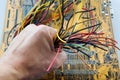 The hand of a man technician holds the bunch of electric wires of different colors are very much intertwined on the background of