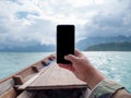 Hand of man using mobile smart phone against scenic landscape of boat view in the big river and reservoir dam with mountain and Royalty Free Stock Photo