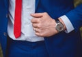 The hand of a man with a hand watch holds on to a blue suit against the background of a white shirt and red tie, a business men`s Royalty Free Stock Photo