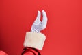 Hand of a man wearing santa claus costume and gloves over red background picking and taking invisible thing, holding object with