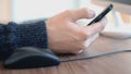 Hand of a man working at computer clicking on mouse and using smartphone