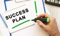 A hand with a marker writes the text SUCCESS PLAN in a notebook on the desktop. Top view Royalty Free Stock Photo