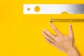 Hand, measure tape and aluminium spirit level tool on yellow background. Construction fluid level with air bubble, flat lay. Royalty Free Stock Photo