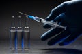 Hand in medical blue glove holding syringe. Grey background. Royalty Free Stock Photo