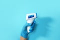 Hand in medical glove with digital infrared non contact thermometer gun for measuring temperature on blue background for Royalty Free Stock Photo