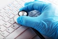 Hand with medical glove holding a stethoscope on computer keyboard. Computer repair service or health diagnosis concept Royalty Free Stock Photo