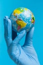 Hand in a medical glove holds a mockup of planet Earth, concept of worldwide danger of viral infection, on a blue