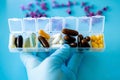 A hand with a medical glove holds multi-colored capsules, a pill box with medicines on a blue background . Royalty Free Stock Photo