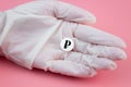 A hand in a medical glove holds a pill with a ruble sign on a pink background. Expensive medicine in Russia. Pharmaceutical