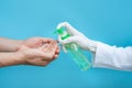 Hand in medical gloves applying sanitize gel onto men hands for protection against infectious virus, bacteria and germs in blue Royalty Free Stock Photo