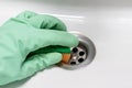 A hand in a mint green rubber glove with an orange sponge rubs the wet dirty white bath or the sink near the drain hole Royalty Free Stock Photo