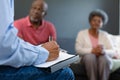 Hand of mixed race senior male counsellor iwth clipboard advising diverse group of senior friends Royalty Free Stock Photo