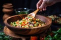 hand mixing couscous salad with diced vegetables using wooden spatula