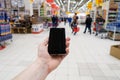 Hand with mobile phone on a background of a blurry shopping center.