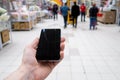 Hand with mobile phone on a background of a blurry shopping center.