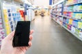 Hand with mobile phone on a background of a blurry shopping center.