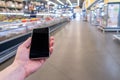 Hand with mobile phone on a background of a blurry shopping center.