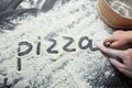 Hand mom and baby write the word `pizza` on the flour, black background.