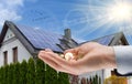 Hand with money against background of house with installed solar panels. Renewable energy and saving money. Conceptual image Royalty Free Stock Photo