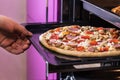 Hand moves the tray of pizza with mushrooms, ham and mozzarella