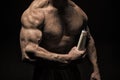 Hand muscular bodybuilder holds plastic bottle. Skin care product. Muscular chest sportsman on black bakground. Product