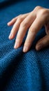A hand with neatly manicured nails rests on a textured blue fabric. The fabric feature Royalty Free Stock Photo
