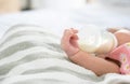 Hand of newborn baby holding and drinking milk from bottle alone on bed at home Royalty Free Stock Photo