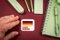 Hand next to Learn German card with Germany flag surrounded by stationery and notebook Royalty Free Stock Photo