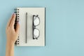 Hand with note pad, eyeglasses and pencil composition on blue background Royalty Free Stock Photo