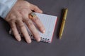 Hand, notepad, gold pen on gray background. Adult man with a sea