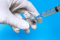 Hand of a nurse in white glove holding syringe and transparent vial on blue background