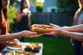 hand offering a hot dog to a friend at a backyard party