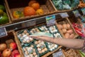 A hand is offering a medical mask in a grocery shop with fresh vegetables and fruits in shelves, details, closeup