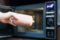 Hand offering raw sausage towards microwave interior for heating. Royalty Free Stock Photo