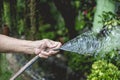 Hand of an old lady holding a rubber hose and blocking the tip to get a spray of water. Outdoor or garden setting Royalty Free Stock Photo