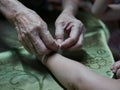 Hand of old woman waving a white string Sai Sin around her granddaughter hands - Thai traditional blessing from an elder one