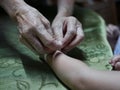 Hand of old woman waving a white string Sai Sin around her granddaughter hands - Thai traditional blessing from an elder one