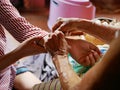 Hand of old woman waving a white string Sai Sin around her granddaughter hands - Thai traditional blessing from an elder one