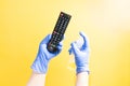 a hand in a one-time rubber glove is spraying a TV LG remote control with an alcohol sanitizer, yellow background, Royalty Free Stock Photo